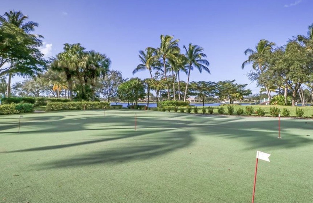 The image shows the Village Walk tennis courts featuring a Har-Tru clay surface, illuminated by professional lighting for evening play, set within a beautifully maintained community in Naples, FL. This sought-after community offers residents access to various amenities, including community pools and a fitness center.