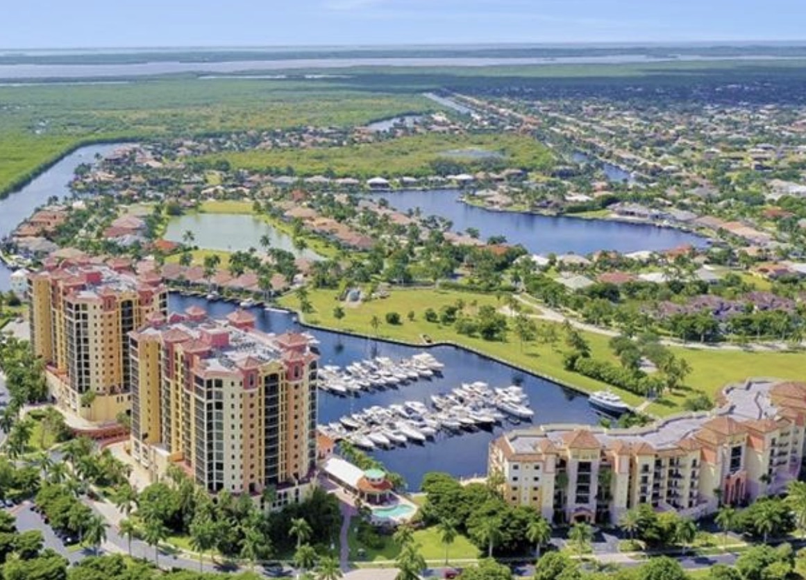 An aerial view of Cape Harbor marina showcases luxury waterfront properties and various boats docked along the scenic canals, highlighting the vibrant yachting community of Cape Coral, FL. The image captures breathtaking views of the marina villas and the surrounding area, perfect for prospective property consumers interested in Cape Harbour real estate.