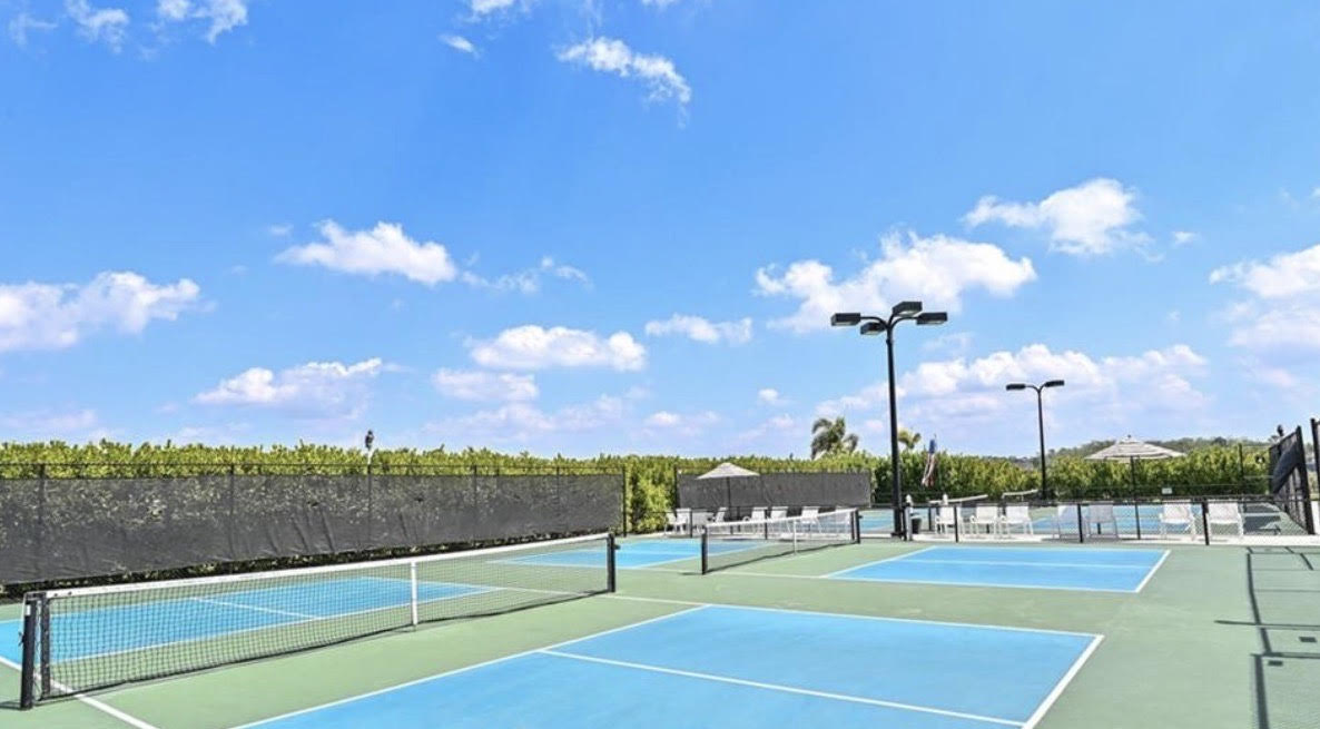 The image depicts a stunning model home featuring coastal-inspired architecture typical of Corkscrew Shores, a master planned community in Estero, Florida. The design highlights modern finishes and is surrounded by lush landscaping, reflecting the community's appeal and beautiful lake views.