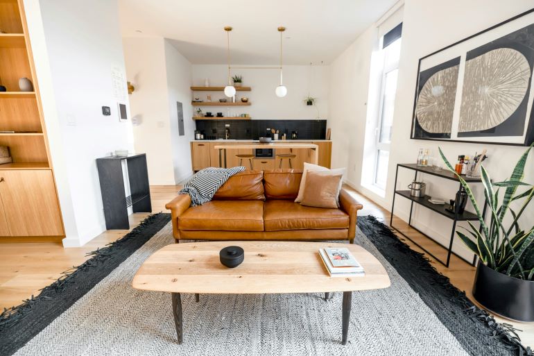Stylish living room featuring a brown leather sofa, wooden coffee table, and open kitchen with modern decor