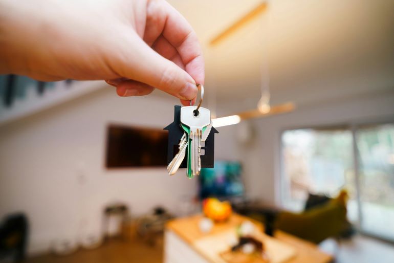 Close-up of a hand holding keys with a house-shaped keychain in a modern living room