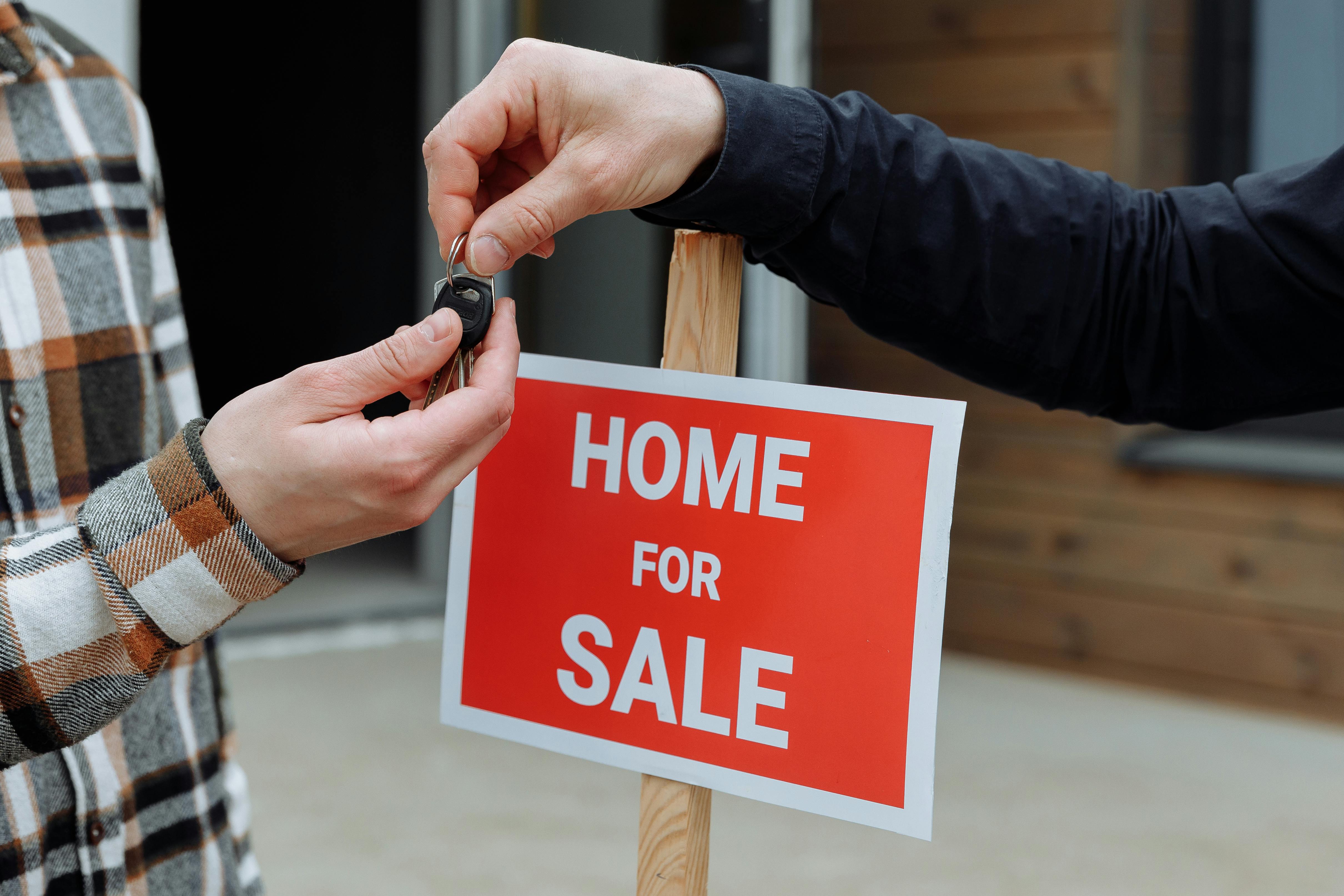 Two people exchanging house keys next to a red “Home for Sale” sign, marking the completion of a property purchase affected by home inspection issues