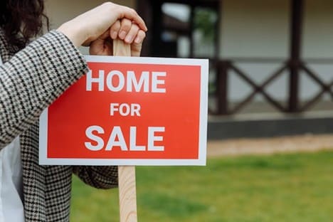 A woman leaning on a red sign in front of a house