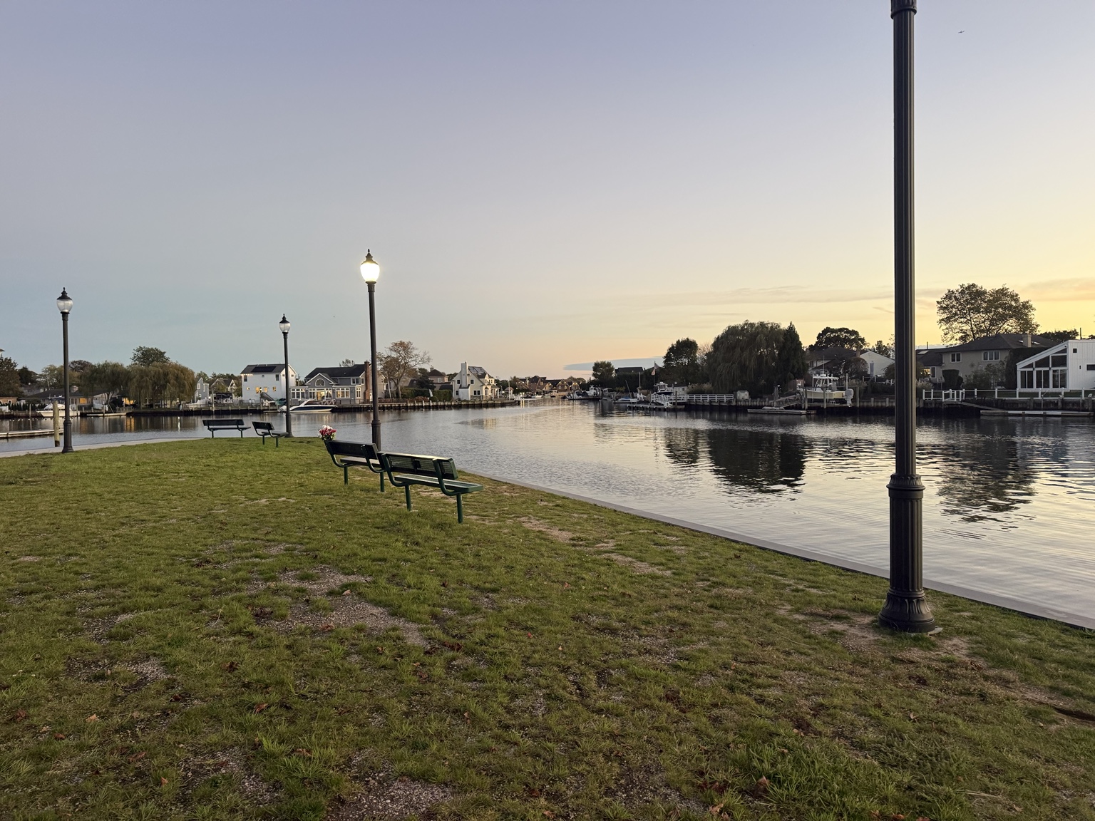 Waterfront canal, green benches and lampposts at John J Burns Park in Massapequa at sunset