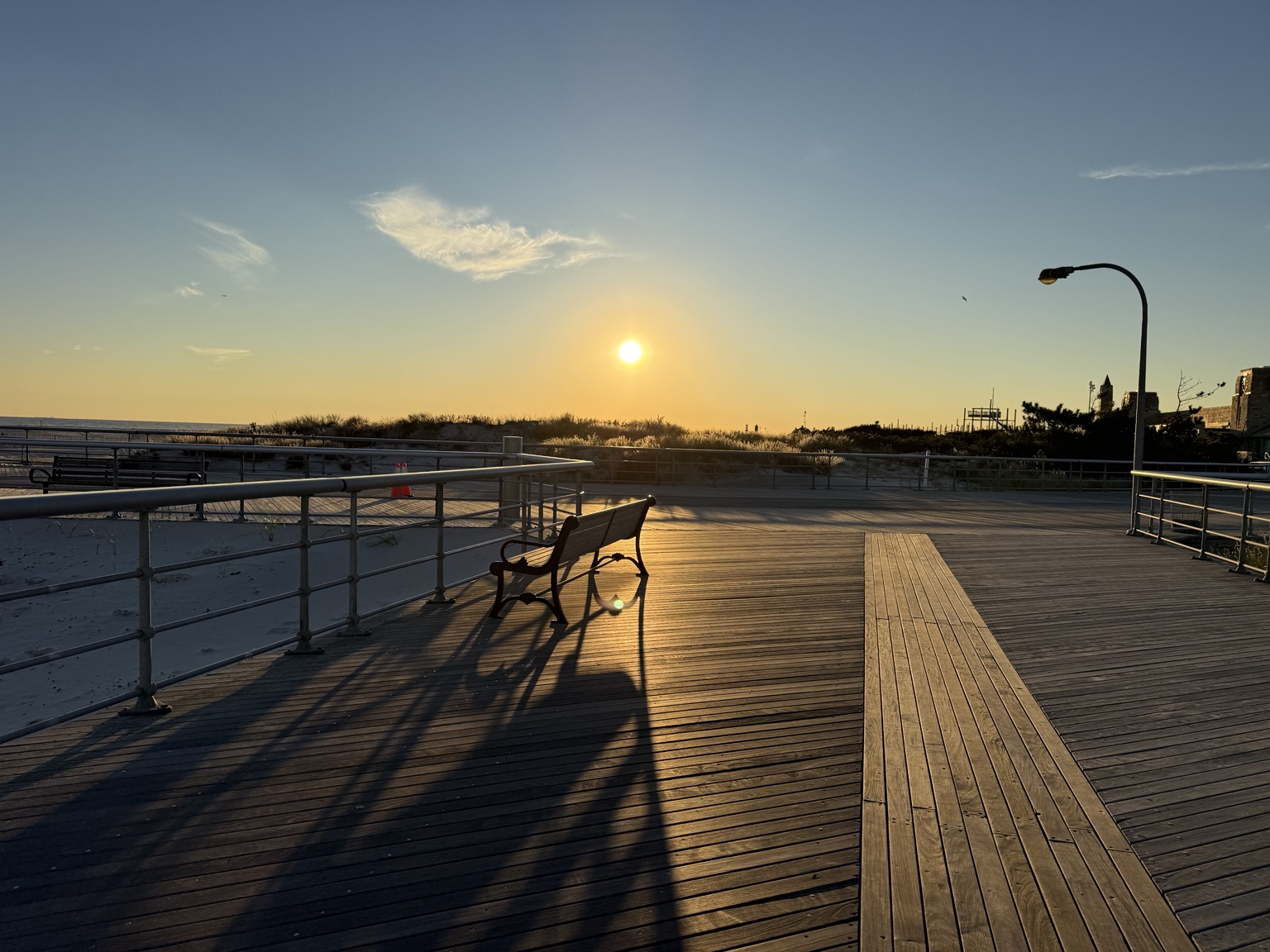 An empty bench and long railing shadows on the Jones Beach boardwalk before sunset