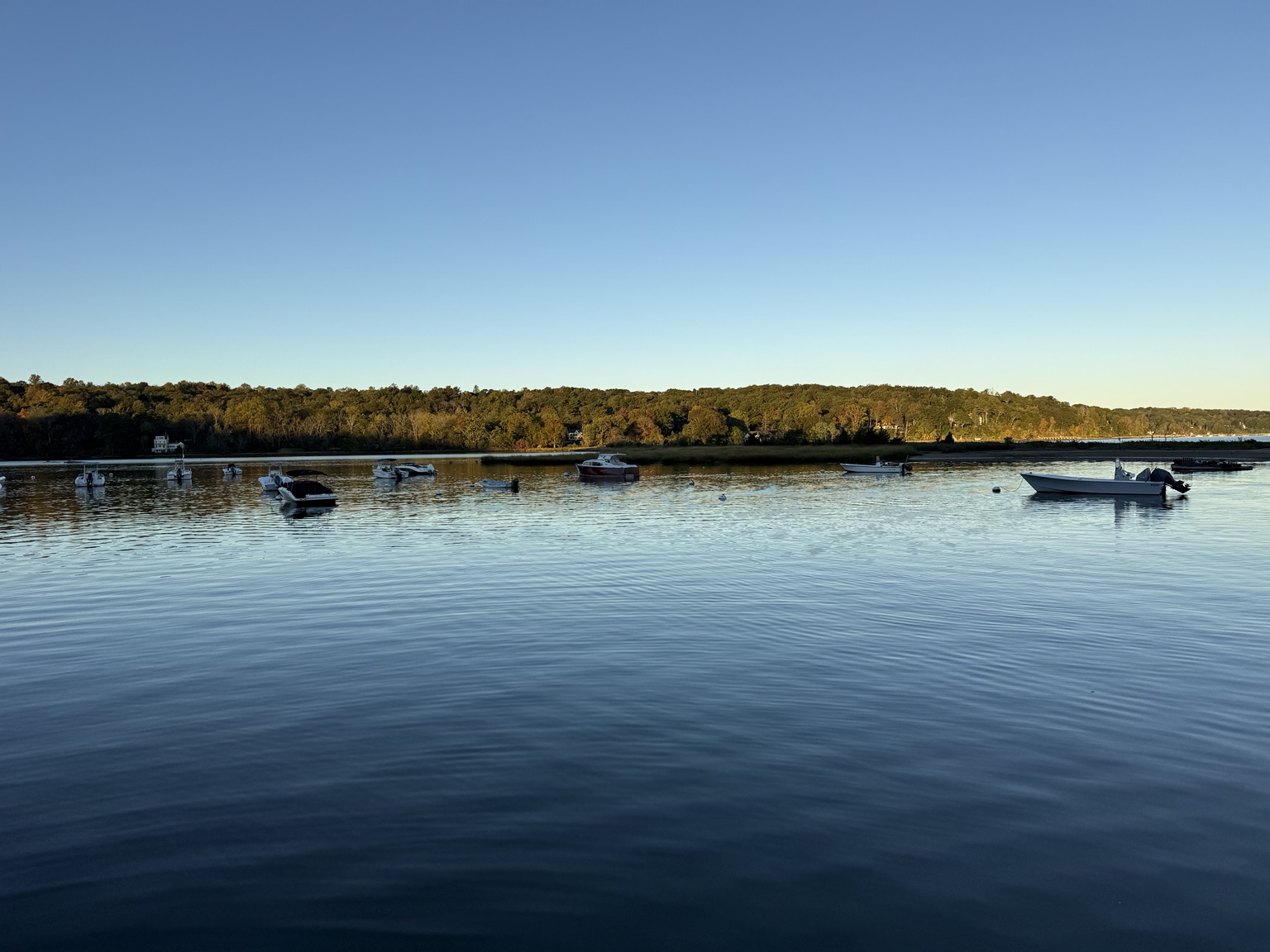 Moored boats and wooded shoreline across Cold Spring Harbor on a clear October morning