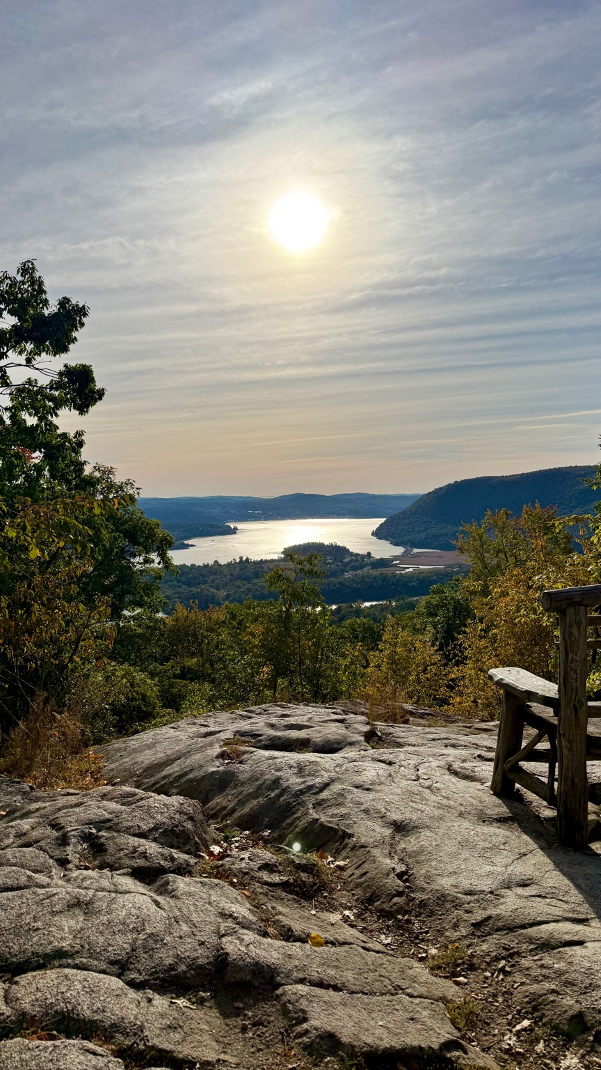 Sunlit Hudson River and forested hills seen from a rocky Appalachian Trail overlook near Bear Mountain, NY