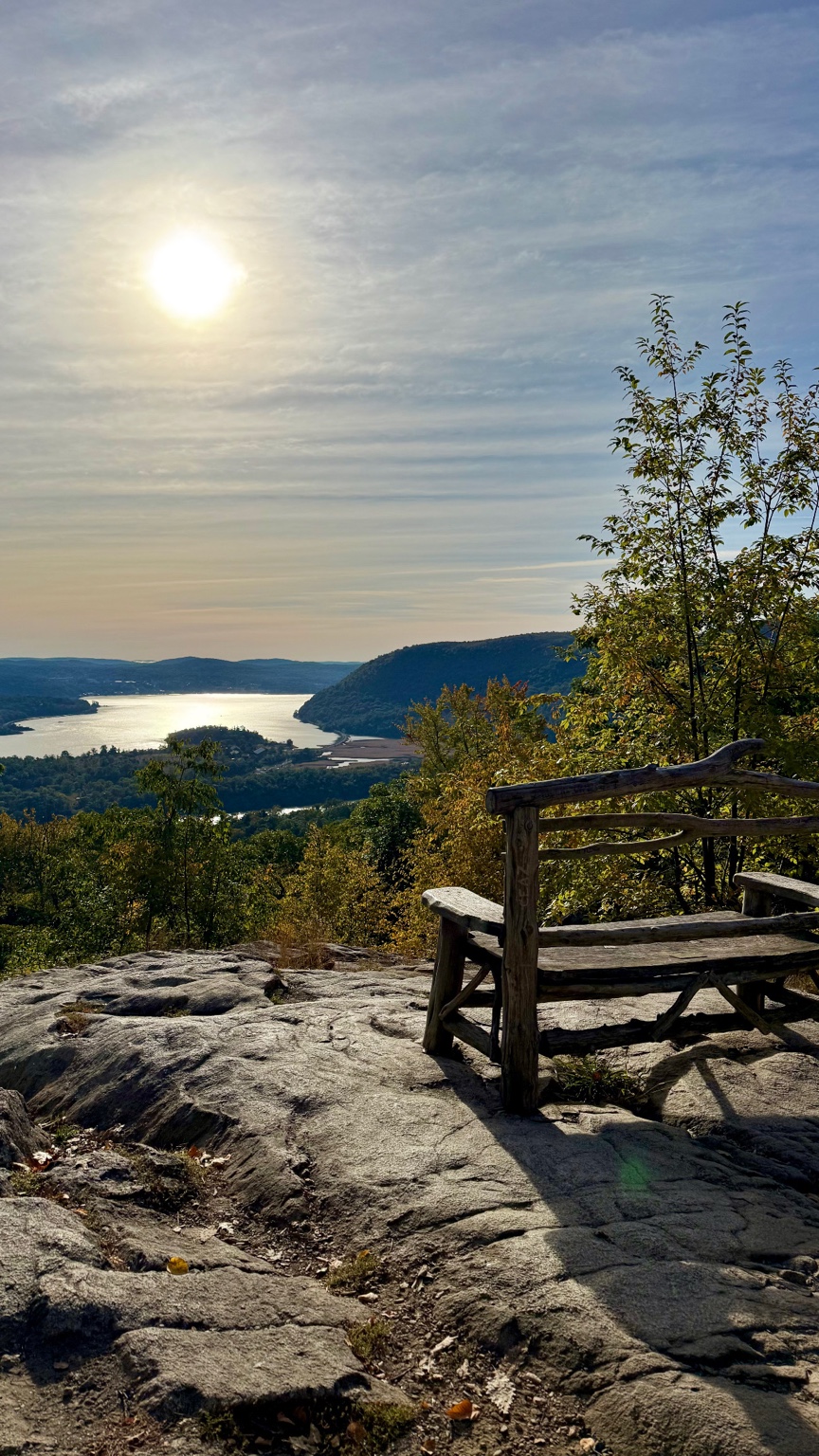 Rustic wooden bench overlooking the Hudson River and wooded hills from a rocky trail near Bear Mountain