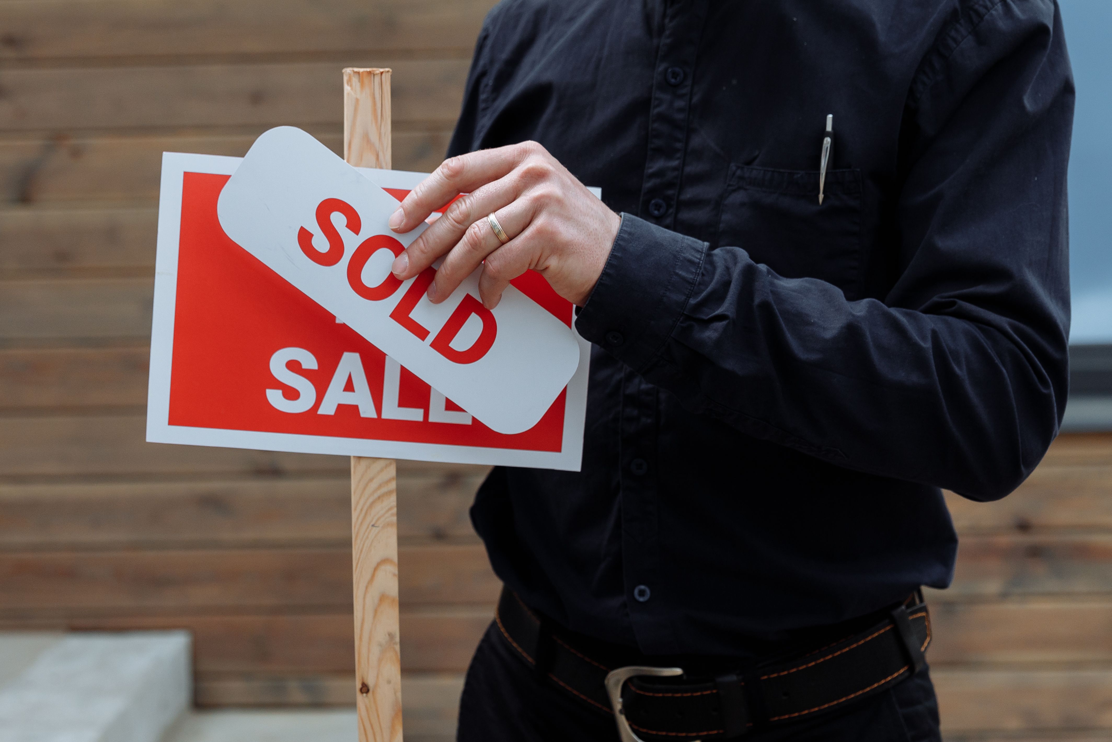 a person sticking a sold sticker on a signboard