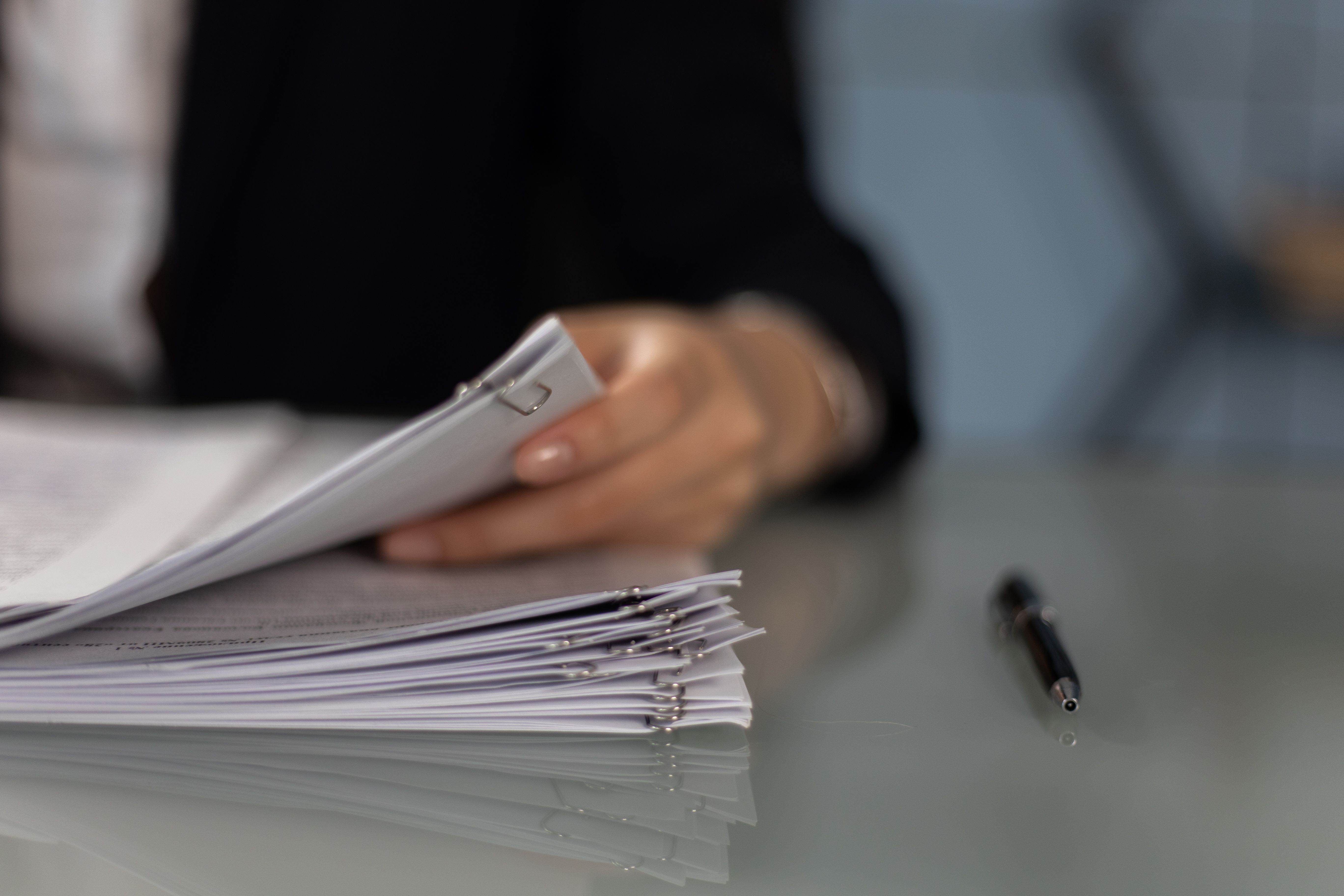 a person holding paperwork beside a pen