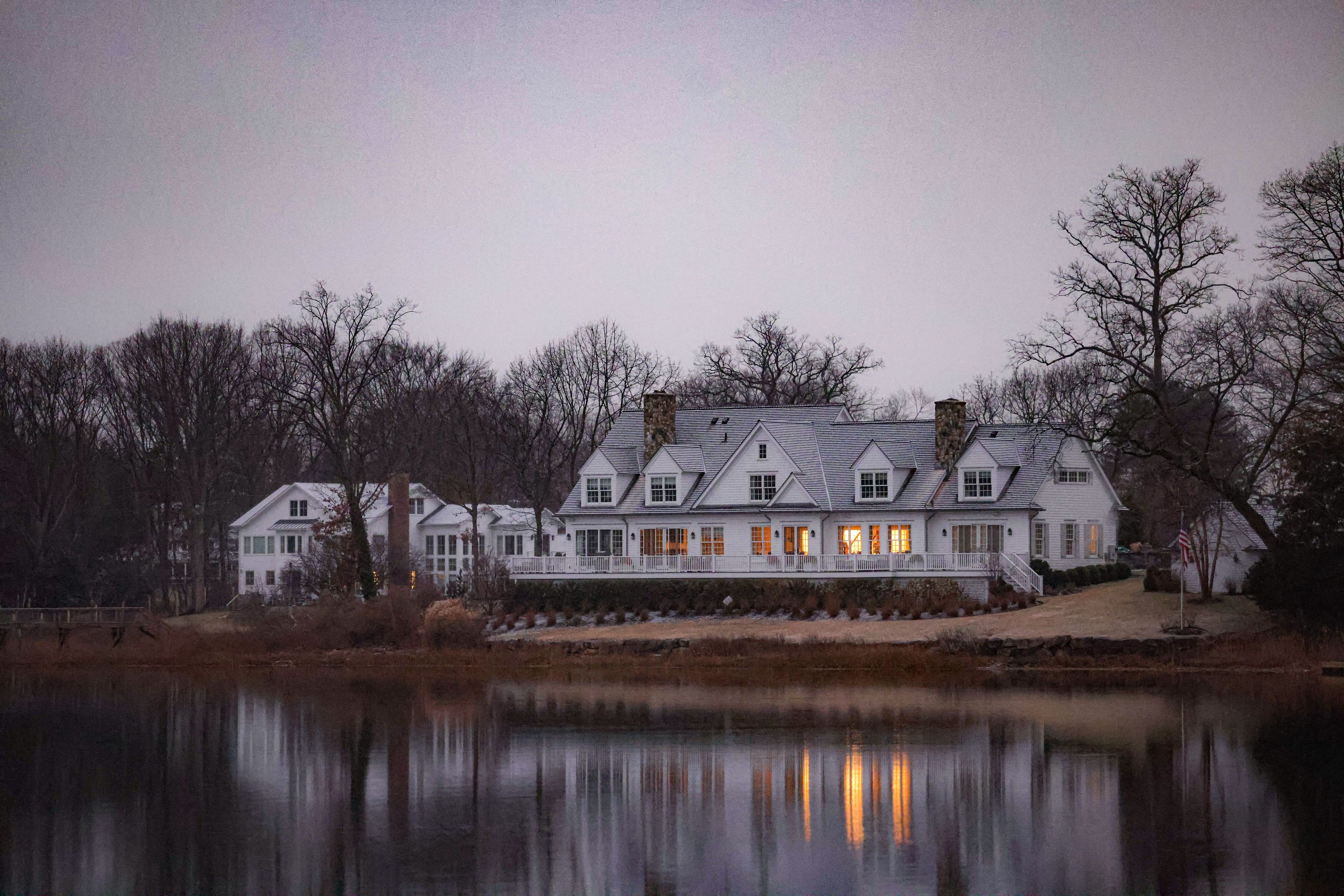 a white house by the lake and surrounded by trees