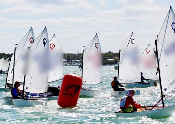 Youth sailors in Optimist dinghies rounding a red racing mark during a youth regatta in Key Largo, Florida