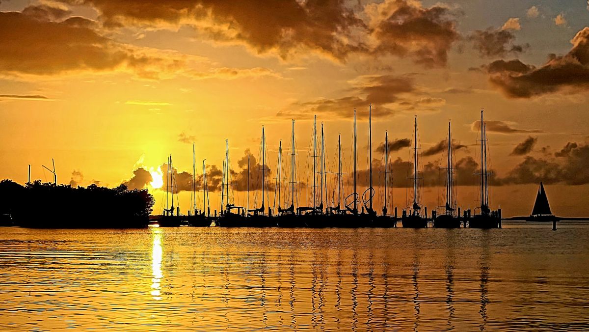 Sunset over Buttonwood Sound with sailboat masts silhouetted along the Upper Keys Sailing Club main dock in Key Largo, photographed by Jim Signor