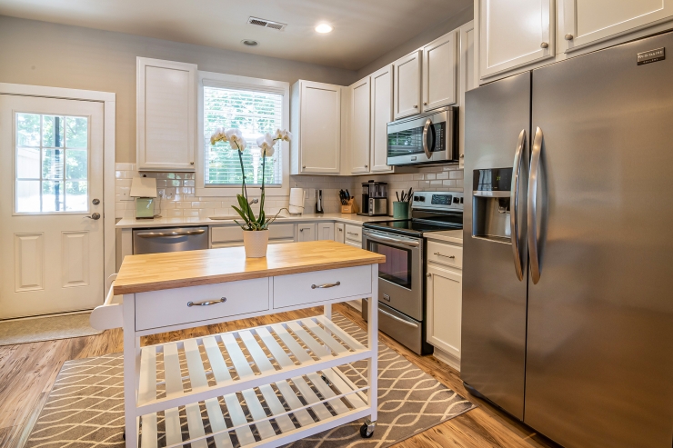 Kitchen with white cabinets, simple hardware, a subway tile backsplash and a rolling butcher-block island.