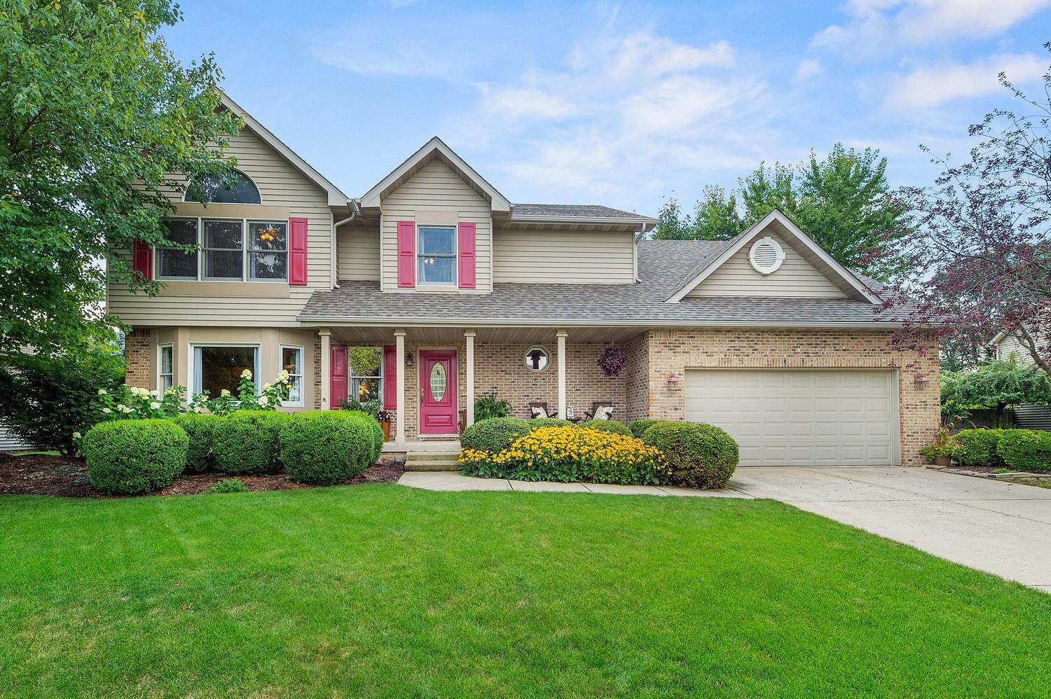 Two-story brick and siding home with a front porch and landscaped beds in Plainfield, Illinois.