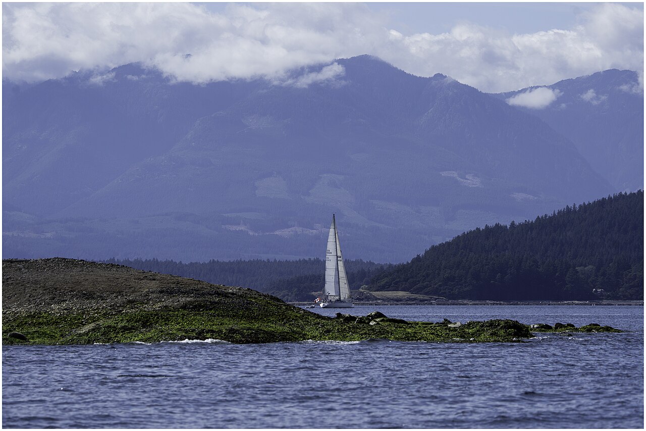 Sailboat on Parksville Bay with forested shore and cloud-topped mountains