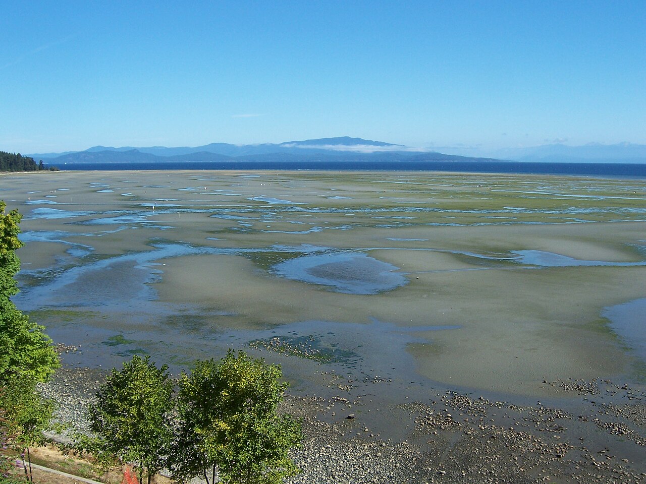Wide sand flats at Rathtrevor Beach in Parksville at low tide with mountains across the water