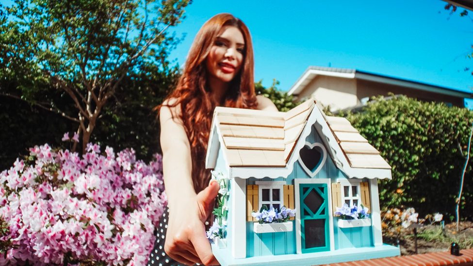A woman holding a small model house outside