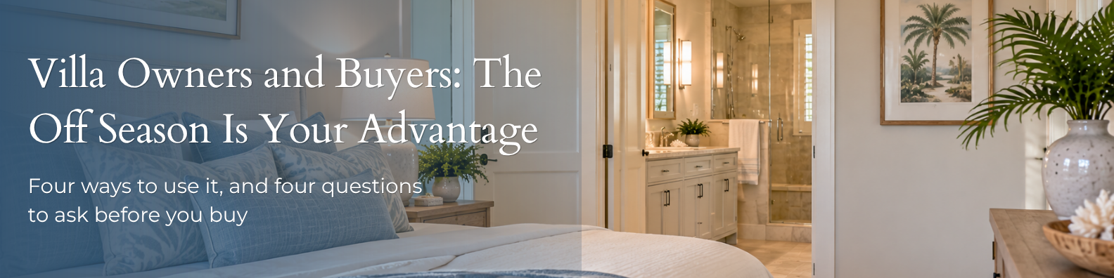 Serene villa bedroom with a bed dressed in soft blue pillows and a lamp on the nightstand, an open doorway to a bathroom with a vanity and glass shower, and a framed palm print on the wall beside a vase of greenery