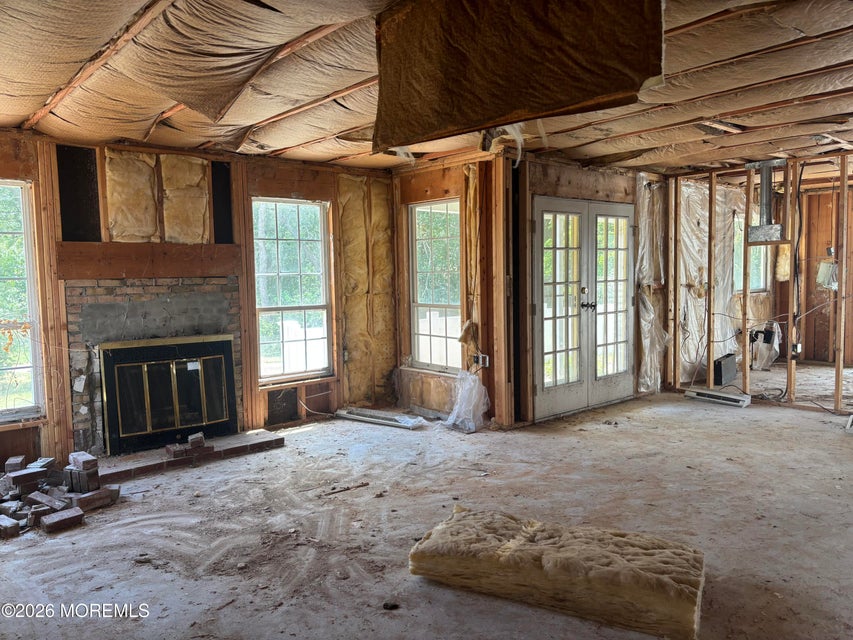 Gutted living room with brick fireplace, large windows, and French doors, stripped to the studs