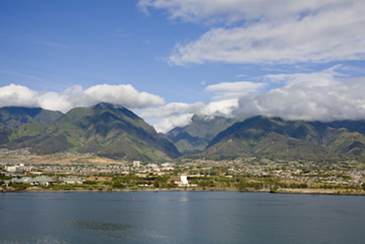 A photo of Kaului's coastline, showing off the blue ocean, rustic Hawaiian city, and looming mountains.