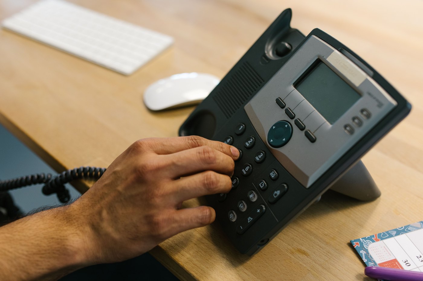 A hand dialing a desk phone beside a planner