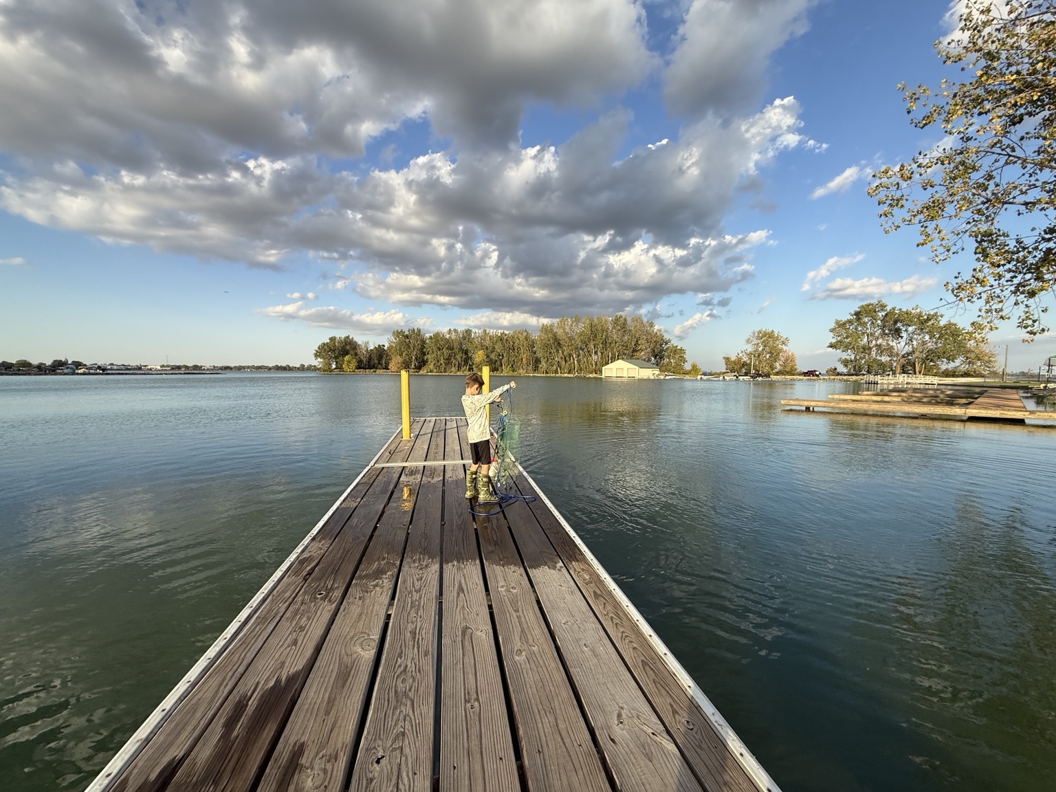 Young angler holding a fishing cast net on a wooden dock overlooking Grand Lake St. Marys Ohio beneath dramatic clouds