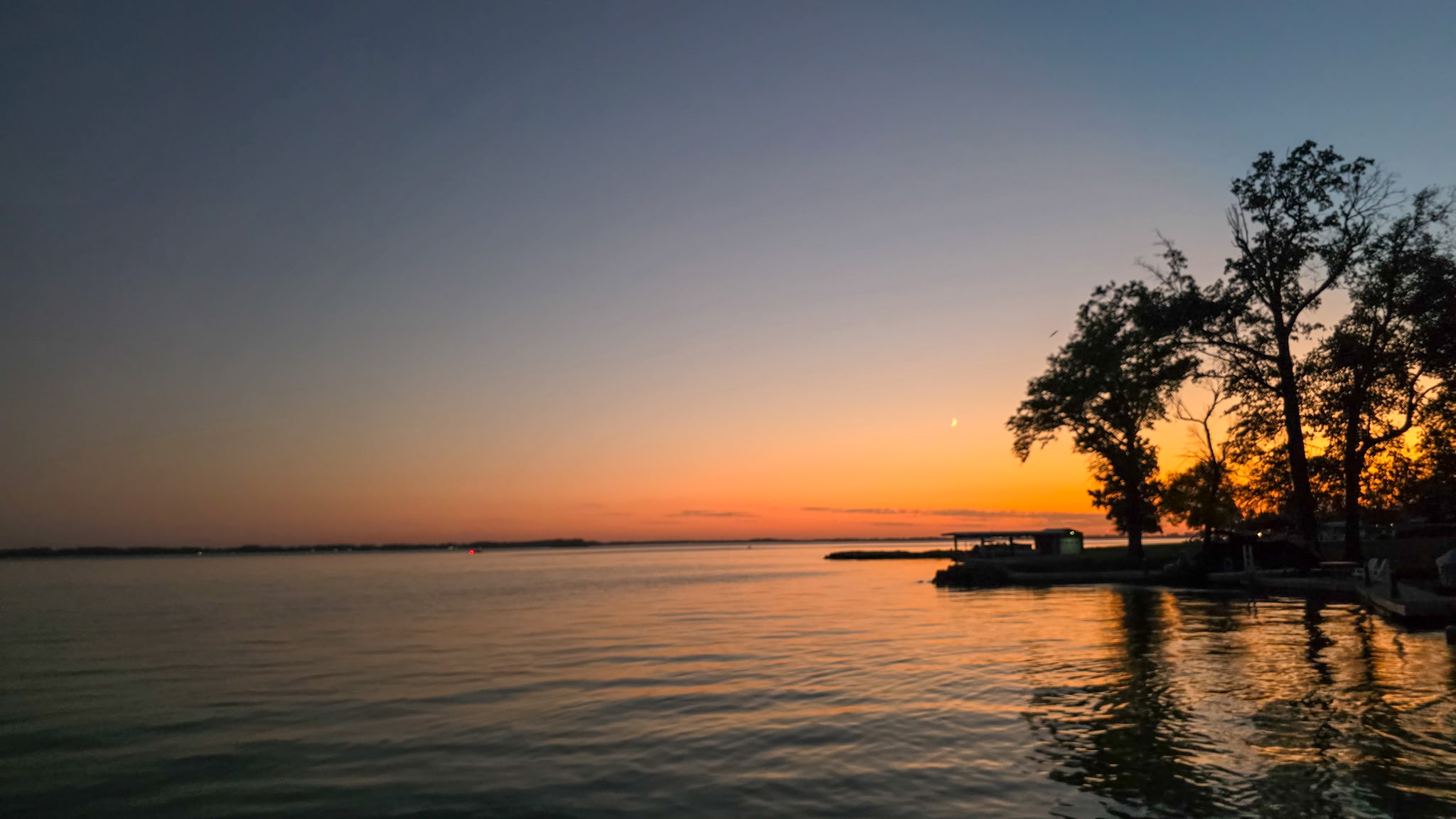 Orange sunset over Grand Lake St. Marys with trees and lakeside docks