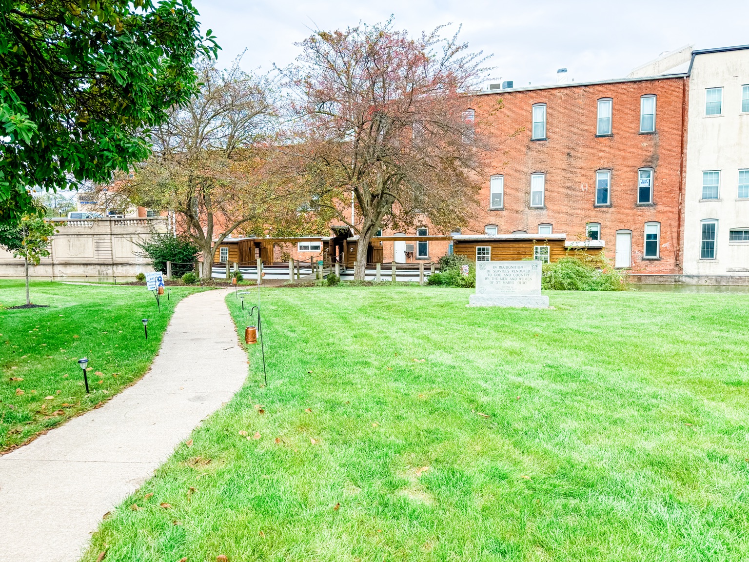 Path through landscaped memorial green space beside historic buildings in St. Marys