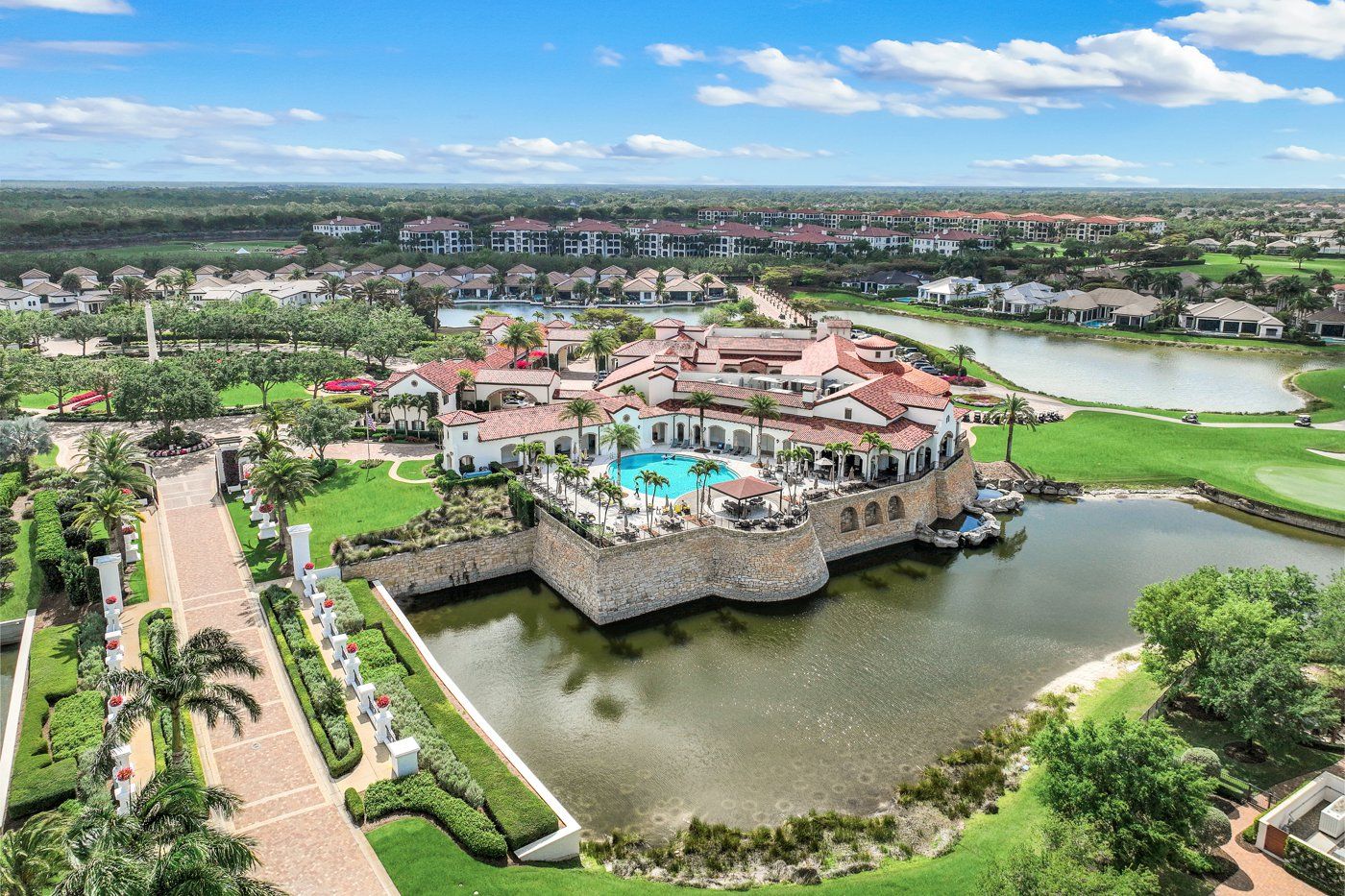Aerial view of the Vyne House clubhouse, pool, and golf course with homes beyond in Talis Park, North Naples, Florida