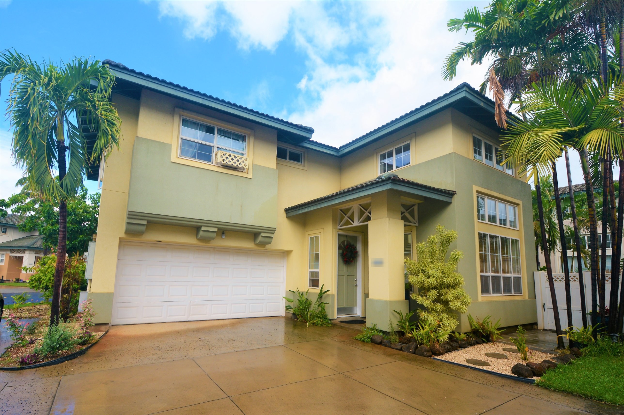 Yellow two-story Kapolei home with a garage and palm trees