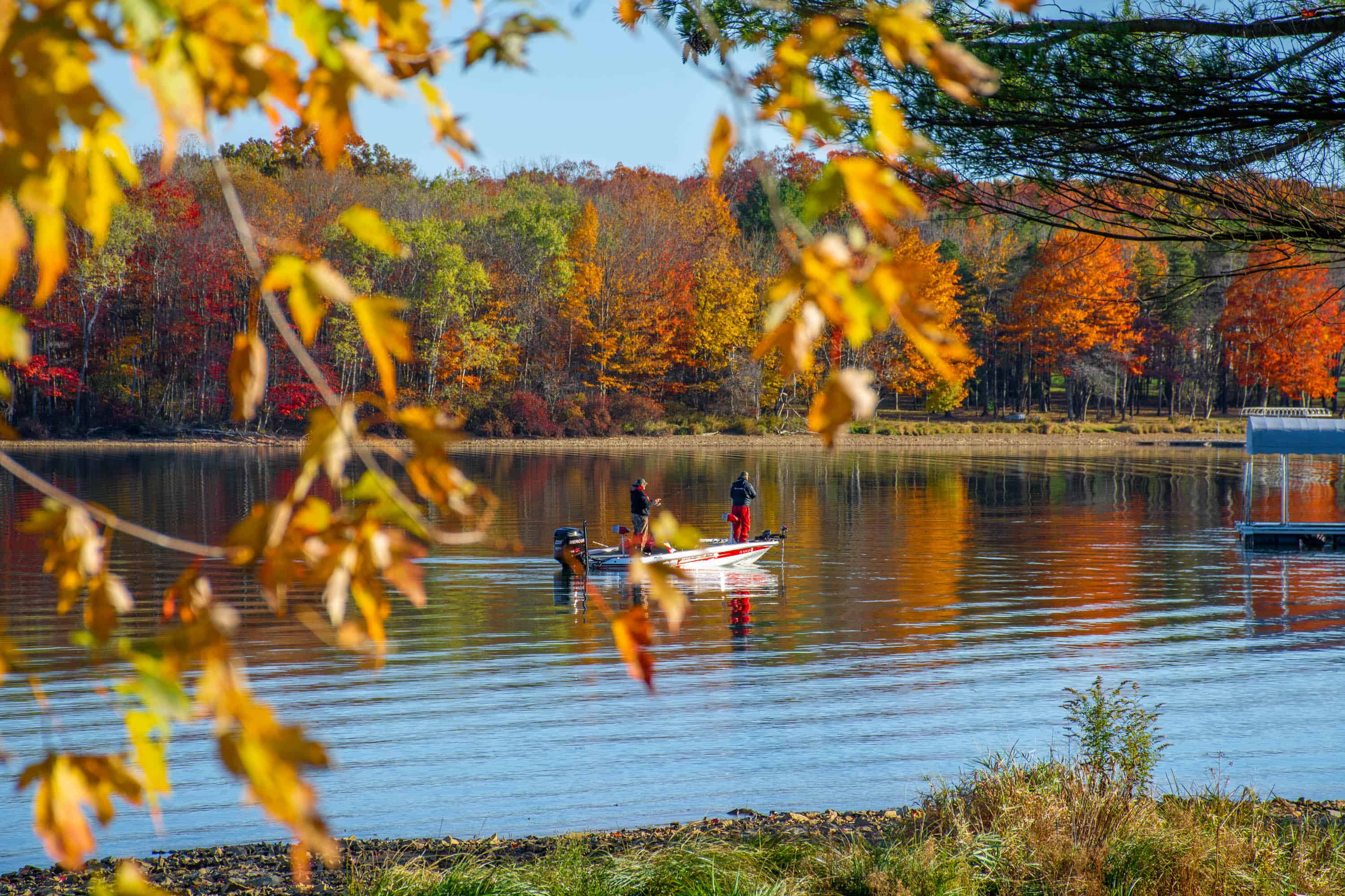 Boaters on Deep Creek Lake with colorful autumn trees along the shore