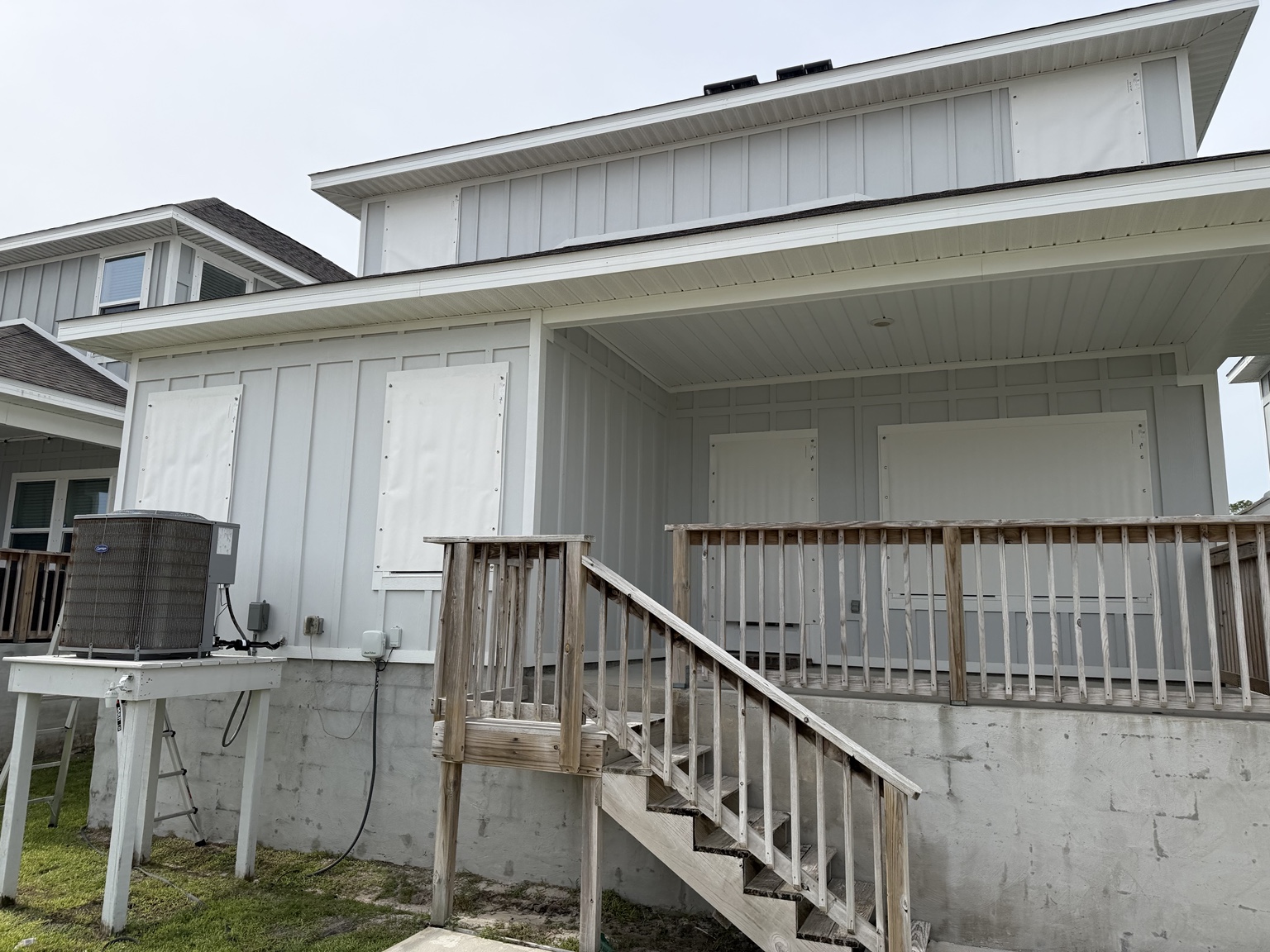 White storm coverings over rear windows and doors beside a vacation home&rsquo;s wooden deck and stairs.