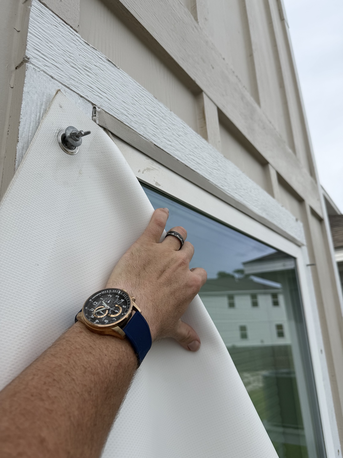 A hand positioning a white covering at a window, with a wing-nut fastener visible above.