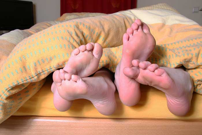 Couple underneath a comforter with their feet sticking out