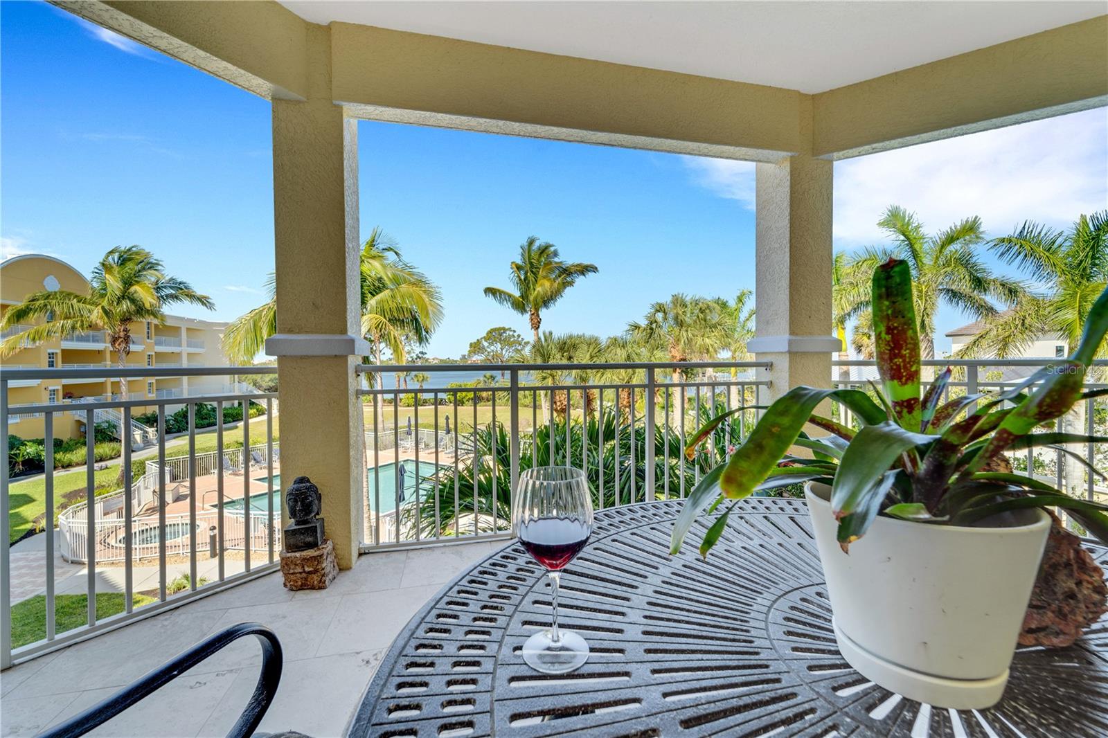 Covered balcony at Bellagio in Osprey, Florida, overlooking a resort-style pool, palm trees and the water