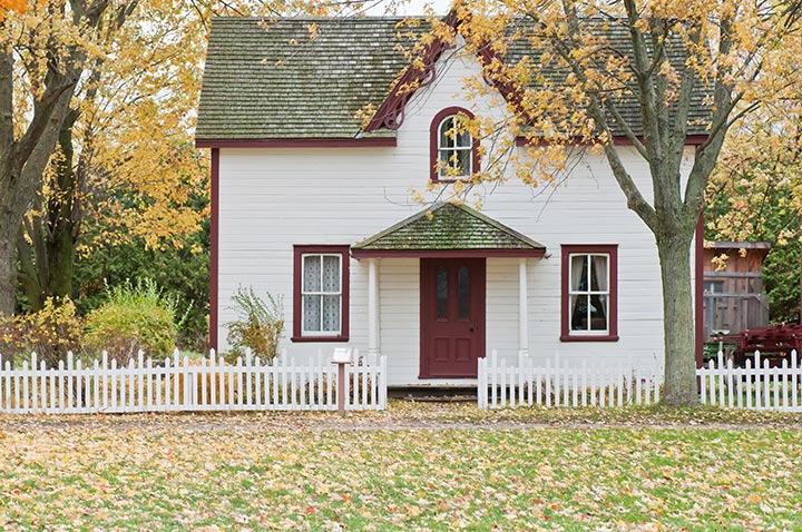 white house with white picket fence and trees surrounding it, all the leaves are yellow and falling to the ground