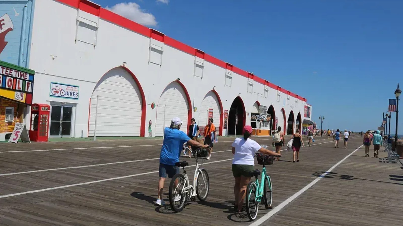 The long white-and-red facade of the former Wonderland Pier along the Ocean City Boardwalk at Sixth Street, with bike riders passing on a sunny day.