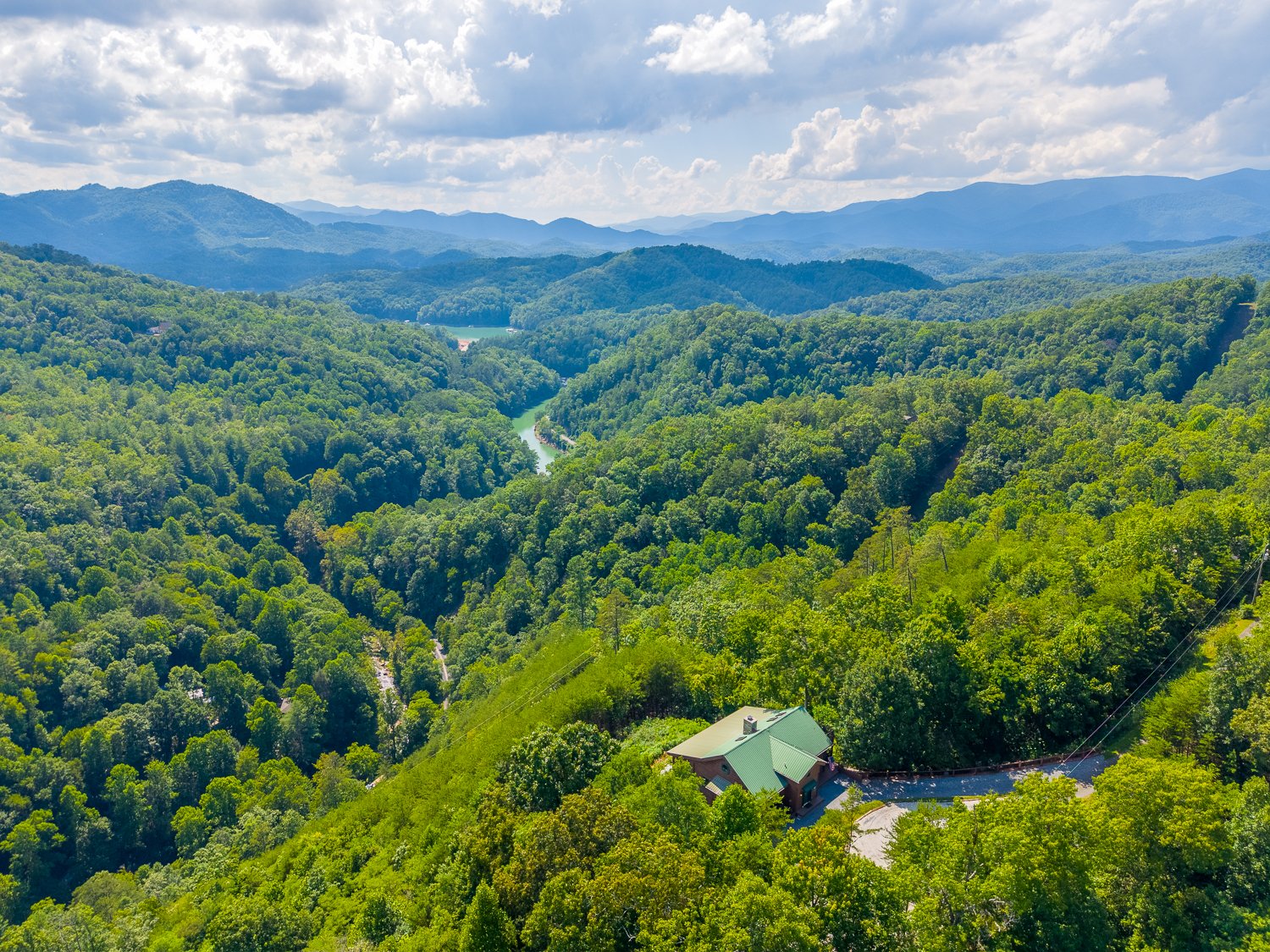 Aerial of the home and wooded acreage with mountain ridges beyond