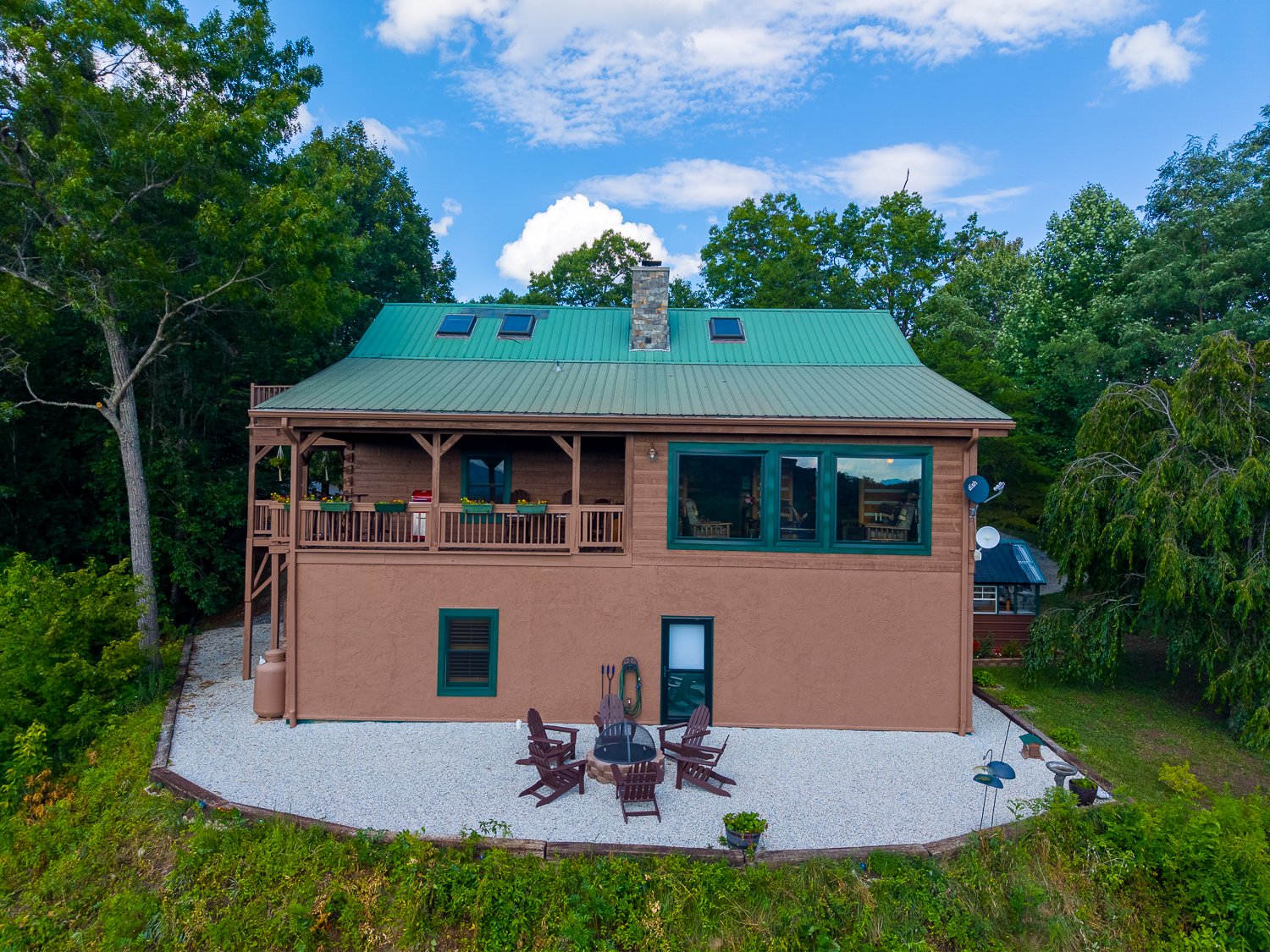 Log home with a green metal roof and wraparound porches on its wooded knoll in Bryson City, NC