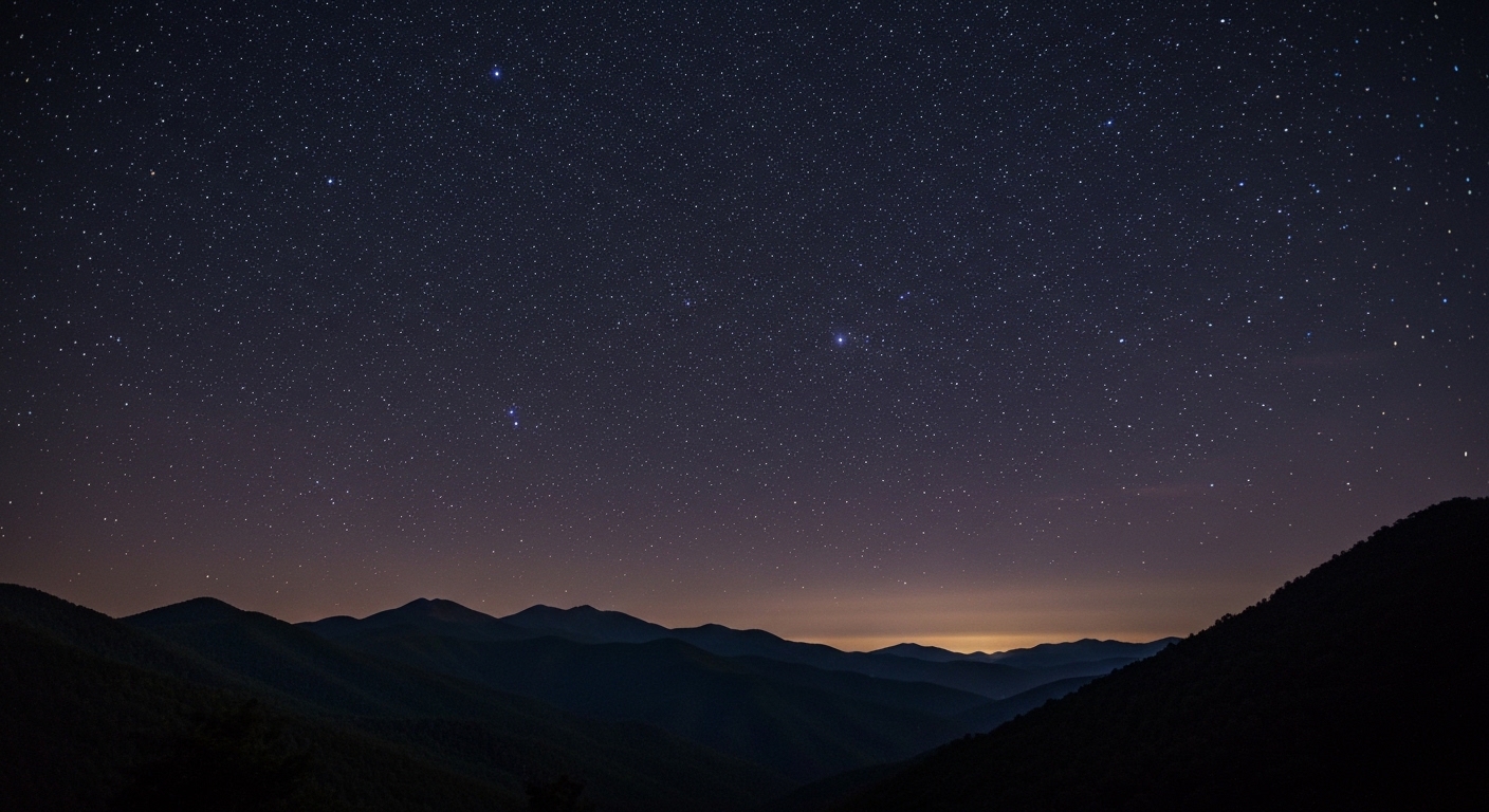 A star-filled Milky Way arching over the dark ridgelines of the Blue Ridge Mountains in Western North Carolina.