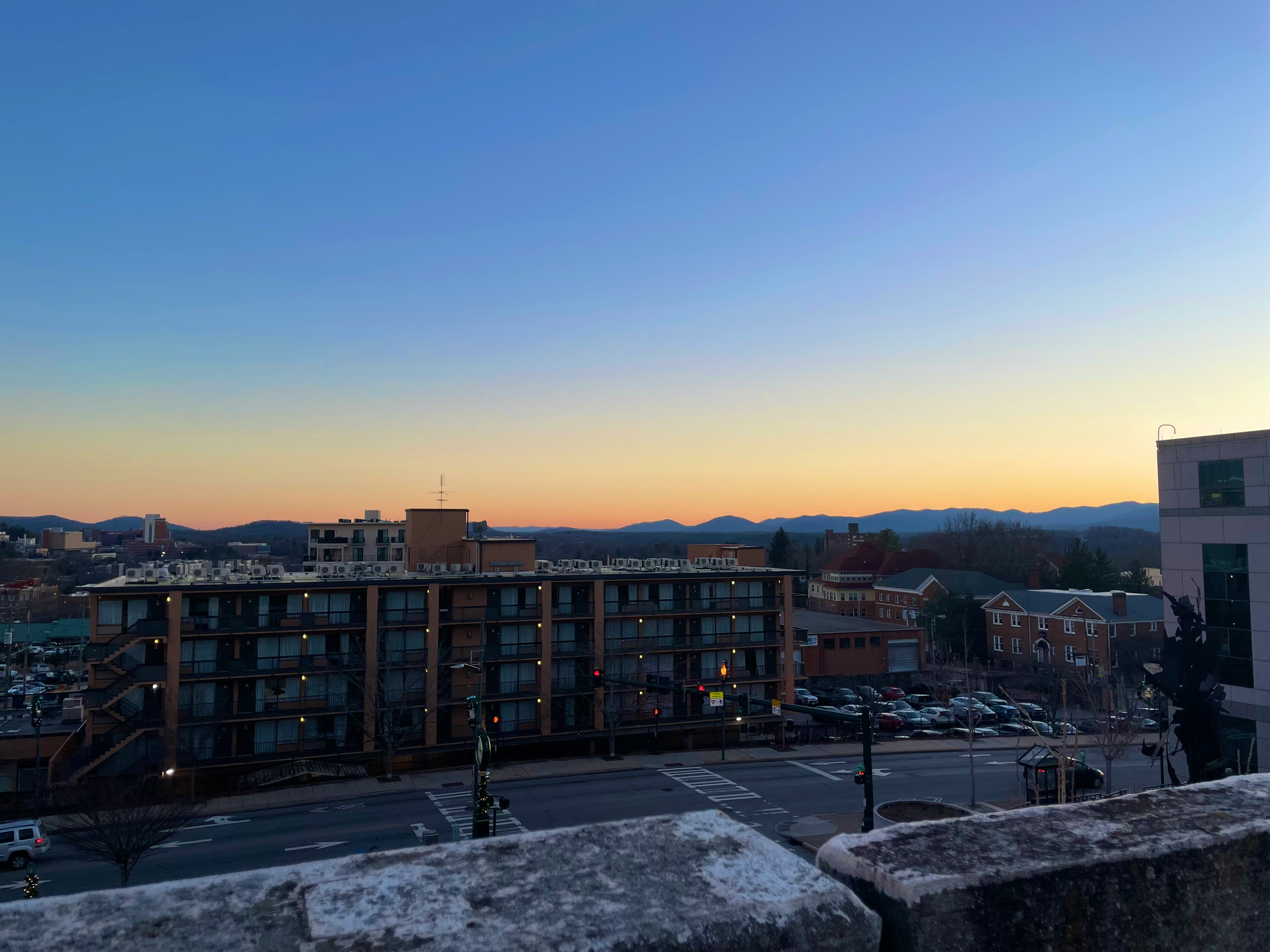 Historic downtown Asheville rooftops and brick towers with the Blue Ridge Mountains rising in the distance at dusk.