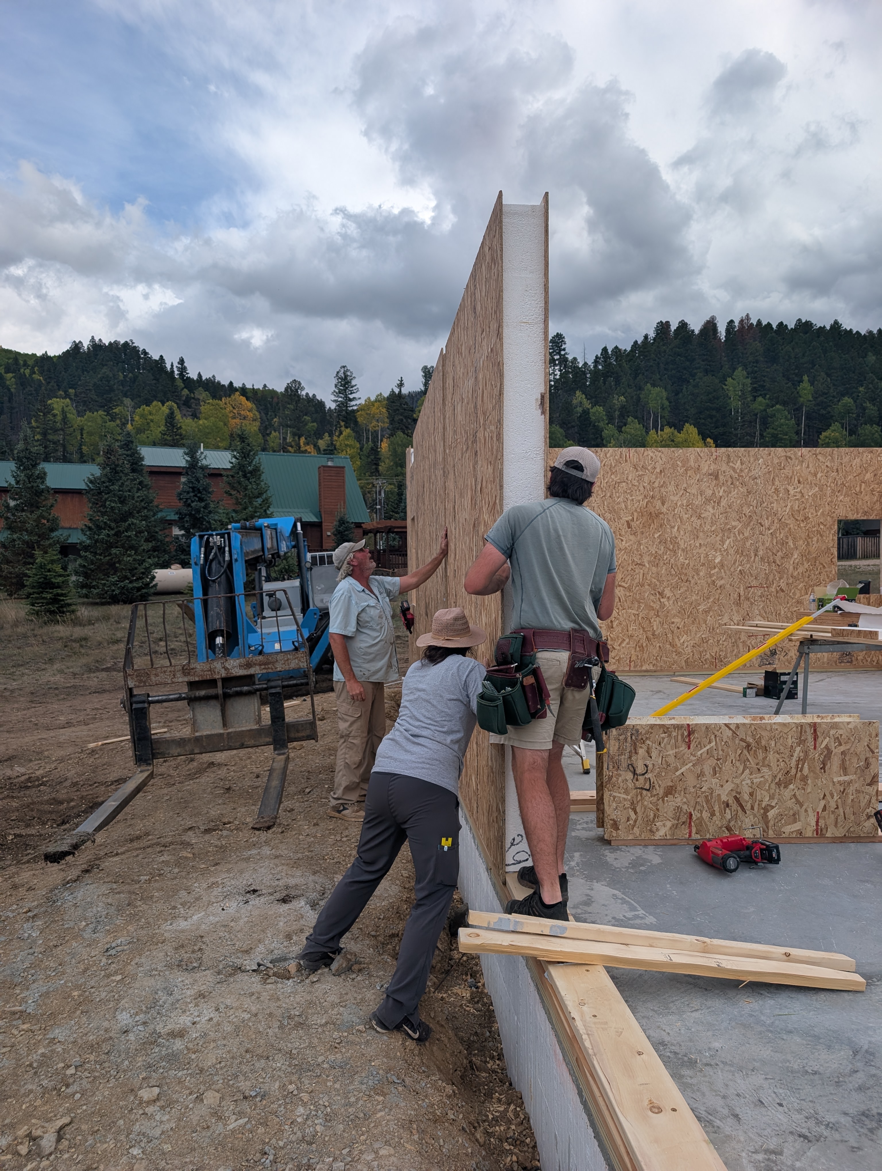 Crew setting a SIP wall panel on a foundation, with forested hills behind