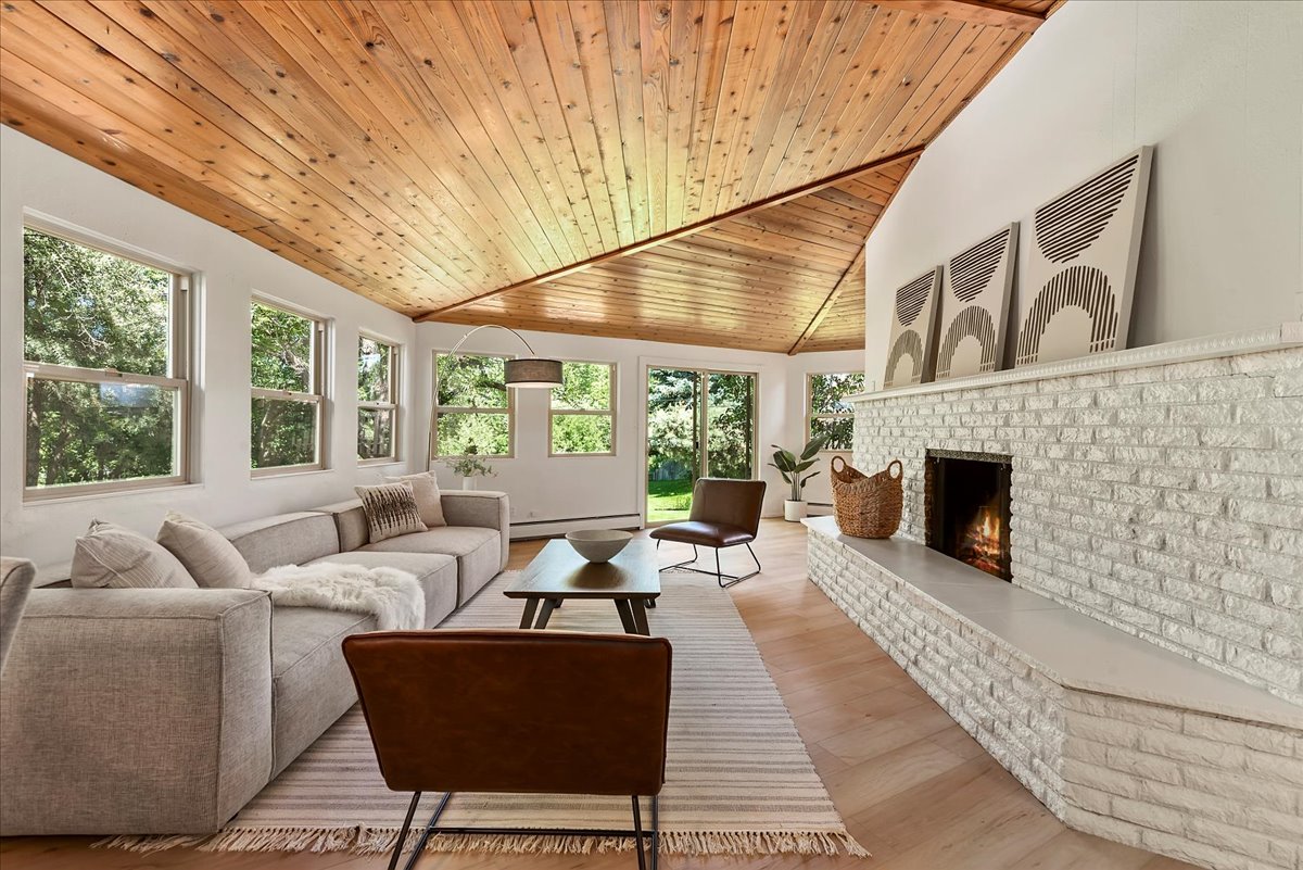 A light-filled living room where warm wood ceilings, natural light, and a cozy fireplace create a calm, welcoming atmosphere.