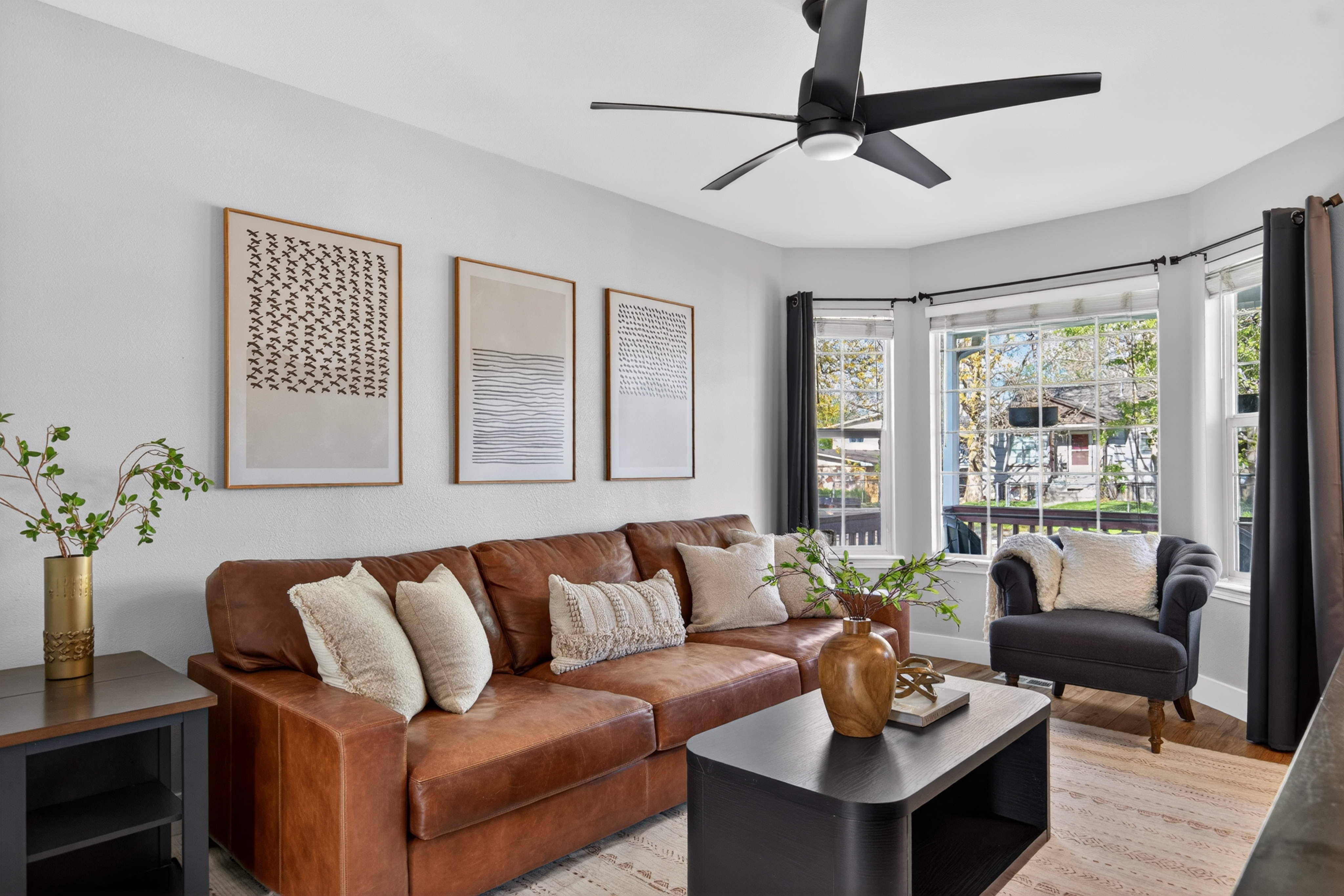 Living room in a Boise, Idaho home featuring a brown leather sofa, hardwood floors, and large windows overlooking the yard.