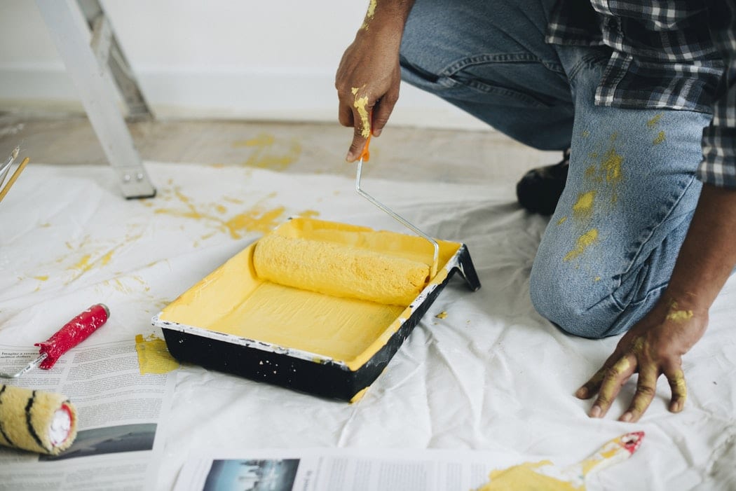 A man rolling a paint roller in a tin of yellow paint.