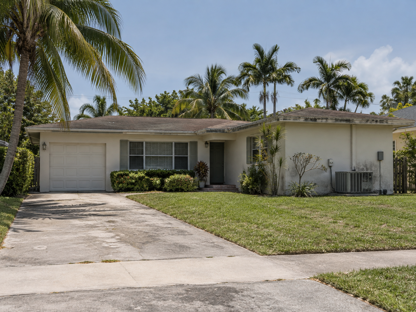 A ranch-style residential property in West Palm Beach, Florida, photographed in flat afternoon light with visible deferred maintenance including an aging roofline and exterior HVAC unit. The scene reflects the common ownership pattern in Palm Beach County where long-term homeowners defer maintenance decisions that later surface during buyer inspections, shifting negotiating leverage. The image supports content addressing seller strategy and preparation decisions before listing.
