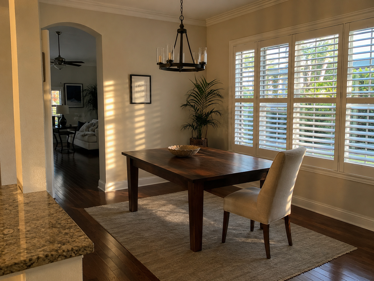 A partially staged West Palm Beach residential interior photographed during late afternoon, with plantation shutters casting linear shadows across an empty dining table. The scene reflects the operational and emotional reality of real estate coordination in Florida divorce matters &mdash; a property mid-transition, ownership unresolved, the space waiting on a legal and logistical process to conclude. Relevant to divorce real estate coordination in Palm Beach County.
