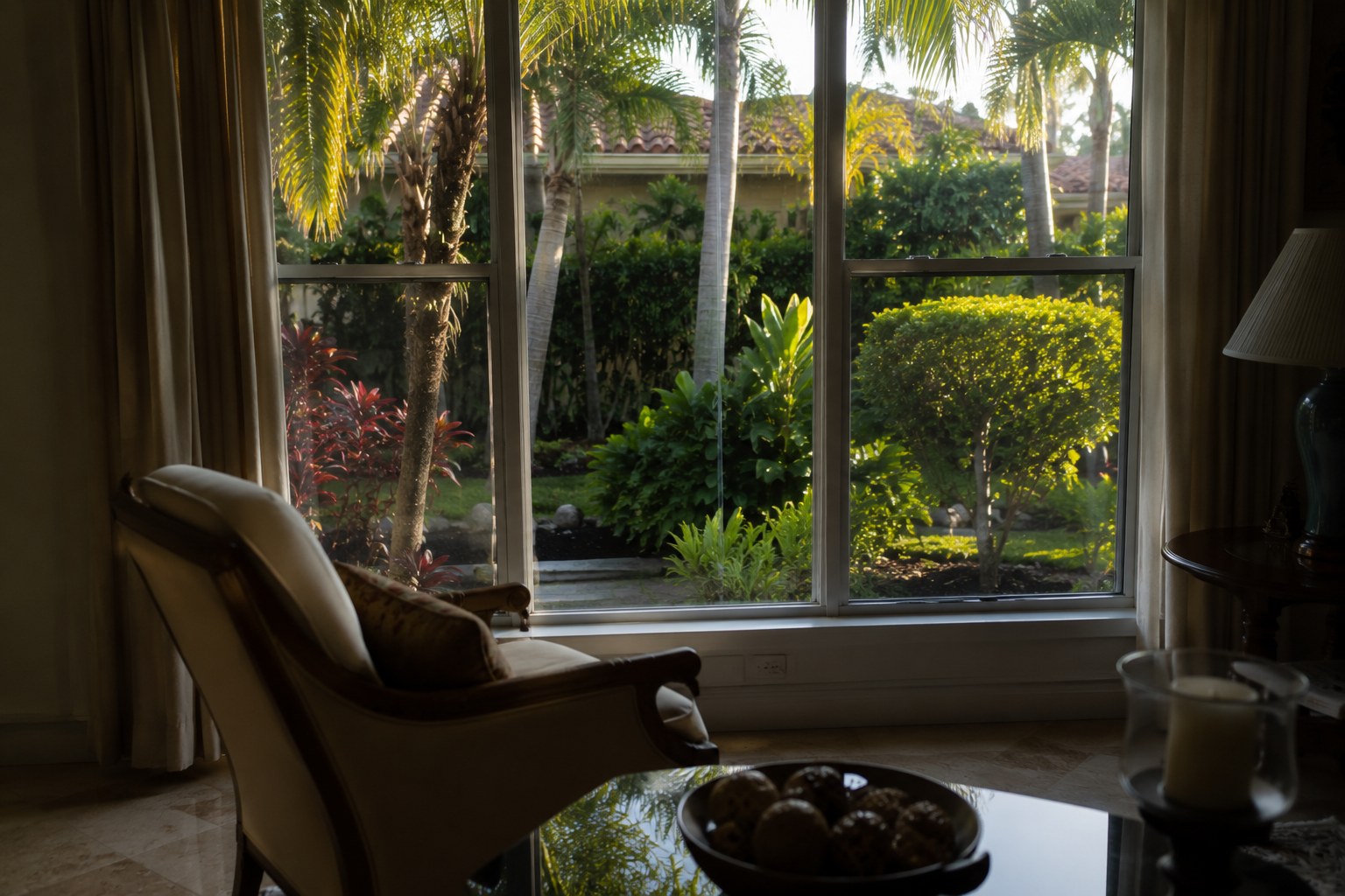 A view from inside a lived-in room through a window onto a mature garden at a Palm Beach County, Florida home in late afternoon light. The scene accompanies an article on the limits of a financial frame in housing decisions, what an ownership analysis can settle, what it cannot, and why the numbers arriving without deciding is information rather than failure.