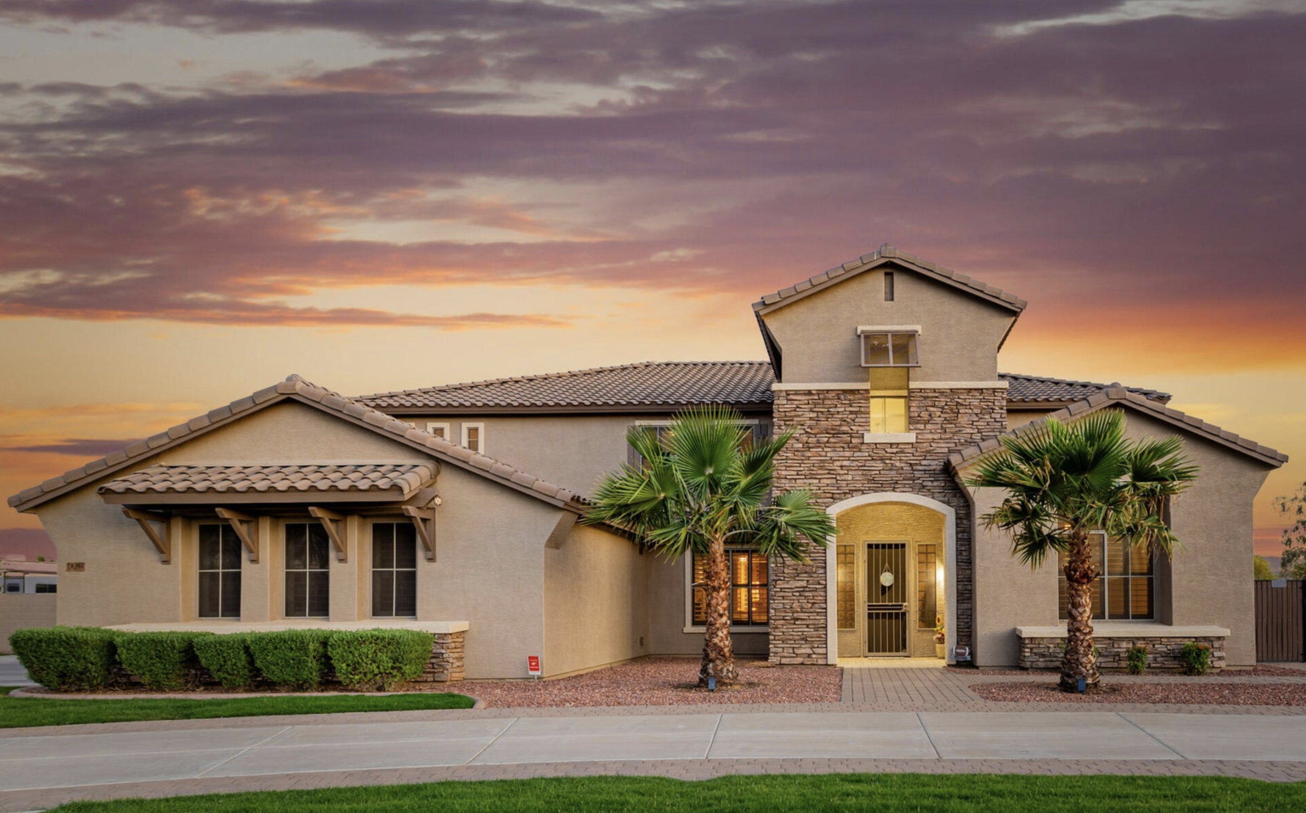 Arizona home with a tile roof, stone-accented entry, palm trees and desert landscaping at sunset.